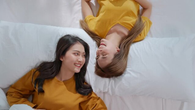 Homosexual lesbian couple lie in bed with their heads collided. Woman and female share love facing each other, smile warmly at each other. Gay family. LGBTQ, LGBT Pride Month, Couple Equality Concept