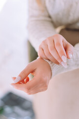 Hands of a young woman on a light background. Manicure with white gel polish