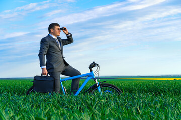 business concept - A businessman rides a bicycle on a green grass field, looks into the distance through binoculars, dressed in a business suit, he has a briefcase and documents
