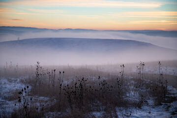 moody winter landscape with fog at sunset