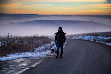 man with his dog in foggy winter landscape at sunset