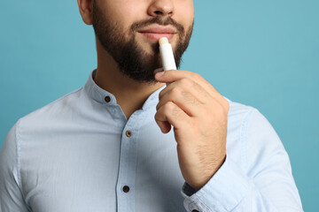 Young man applying lip balm on turquoise background, closeup - obrazy, fototapety, plakaty