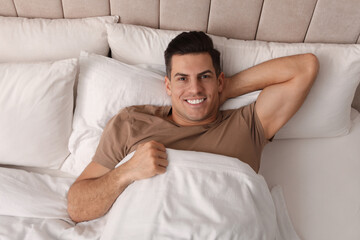 Happy man lying in bed at home, top view