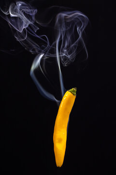 Yellow hot Mexican chili peppers against a black background with smoke coming from it, depicting it to be smoking hot. High quality photo
