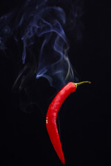 Red hot chili peppers against a black background with smoke coming from it, depicting it to be smoking hot. High quality photo