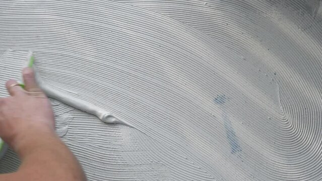 Worker Using Scraper To Smear Glue On Floor Before Gluing Vinyl Laminate Tiles