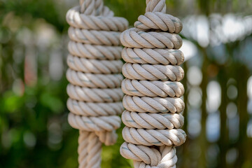 Selective focus of rope tied in knot on swing with green garden as background, A rope is a group of yarns, plies, fibers or strands that are twisted or braided together into a larger and stronger form - obrazy, fototapety, plakaty