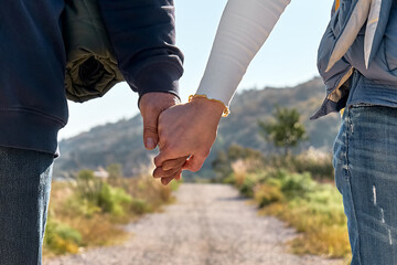Closeup of loving couple holding hands while walking on rural road in autumn or spring nature. Friendship and relationship concept. Well Being and unity with nature. Road to mountain.