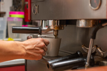 Close-up of a white cup placed in a coffee machine while it is being filled