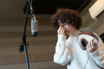 A young curly hair singer woman with a headache recording a song in a studio - obrazy, fototapety, plakaty