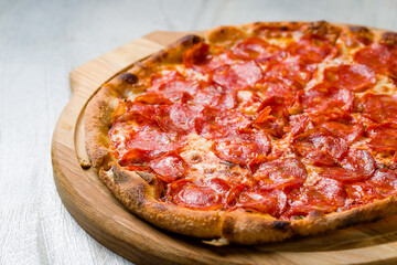 Pepperoni pizza on wooden board on grey table macro close up