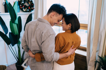 Man and woman hug and stand near window at home