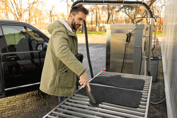 Man cleaning auto carpets with vacuum cleaner at self-service car wash