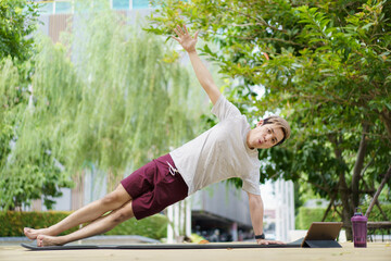 Fototapeta premium Active sportsman doing a side plank exercise and making a video call with a friend.