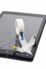 A team of miniature workmen repairing a broken mobile phone tablet touchscreen with a roll of sticky tape