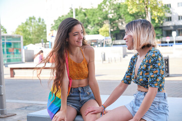 Fototapeta na wymiar Young lesbian couple flirting and smiling sitting on a bench outdoors.