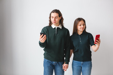 Couple in green shirts holding phones in hands on white background. Young man and woman using phones and laptop. Modern technology