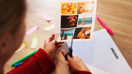 Young woman creating Feng Shui wish map using scissors. Blond cut out photos for visualization of...