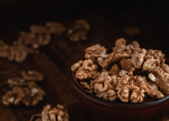 Walnut kernels close up in a brown ceramic bowl on a dark wooden background.