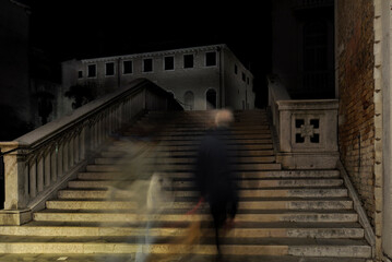 Dos personas de espaldas subiendo una escalera de noche en Venecia semejando espectros por el...