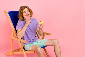 Portrait of handsome trendy cheery guy sitting in chair using device thinking post 5g isolated over pink pastel color background