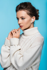 Young woman in knitted sweater using earphone isolated on blue.