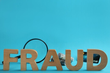 Word Fraud made of wooden letters near money, credit card and magnifying glass on light blue...