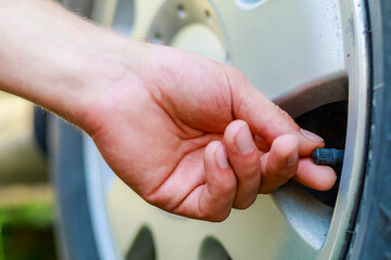 The hand twists or unscrews the nipple cap from the car wheel. Place the air replenishment tires.