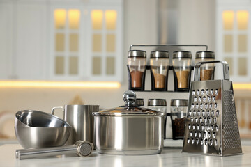 Set of shiny cooking utensils and spices on white table against blurred background