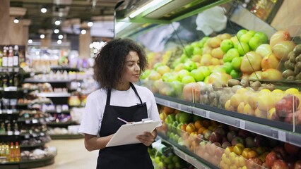 Portrait of african american female staff person standing in front of the fruit shelves with tablet