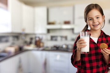 Portrait of sad girl holding glass of milk and dreaming, sitting on dinning table in kitchen interior