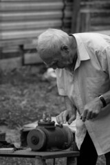 An elderly man, during repairs in the summer at the cottage, sharpens a knife on a grinding machine. Black and white image. Banner, cover, flyer, layout design.