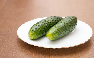 two green cucumbers lie on a white plate