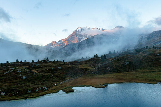 Aerial view of Fletschhorn and Galehorn mountains in fog at dawn from Hopschusee lake, Simplon Pass, Valais canton, Swiss Alps, Switzerland