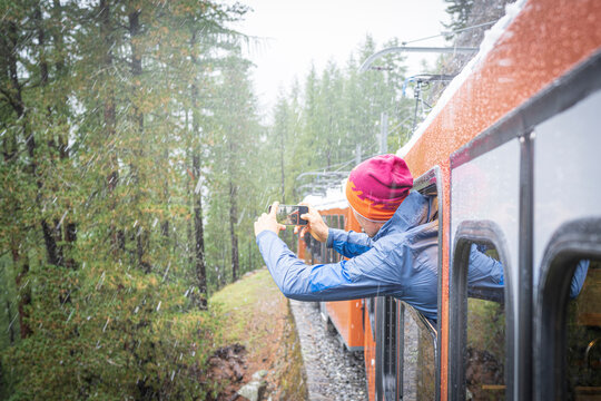 Man photographing the snow falling over the forest leaning out of Gornergrat Bahn train, Zermatt, Valais canton, Switzerland