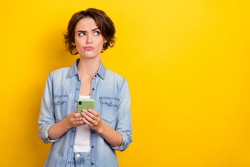 Photo of young woman look empty space unsure use cellphone app 4g isolated over yellow color...