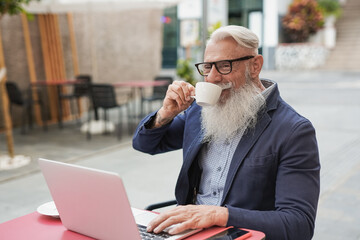 Senior business man drinking coffee while using computer laptop at bar outdoor