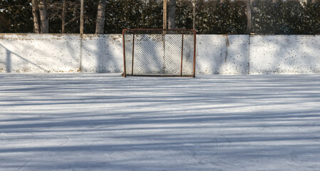 Outdoor hockey rink showing ice surface, end boards, and an empty goalie's net, daytime, nobody