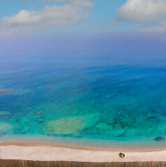 Vista desde lo alto de una pequeña playa en el mar Tirreno (Italia) de un mar turquesa de aguas transparentes. En la playa cercada por una cerca de juncos se destaca una sola sombrilla de colores.