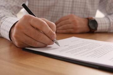 Businessman signing contract at wooden table, closeup of hands