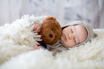 Sweet baby boy in bear overall, sleeping in bed with teddy bear