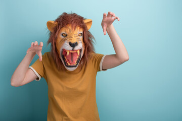 Young woman in lion mask making scary attack gestures with hands, isolated on blue background with...