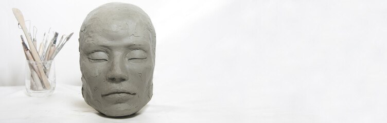 Isolated head sculpture and handmade art tools on white background. Portrait of female mask for art instruction and workshop.