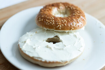 Close up of a bagel with cream cheese on a wooden cutting board.