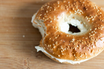 Close up of a bagel with cream cheese on a wooden cutting board.