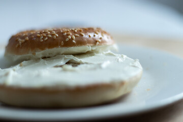 Close up of a bagel with cream cheese on a wooden cutting board.