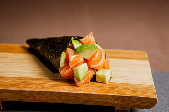 
Sushi temaki freshly prepared with salmon and avocado. Japanese food in a wooden background. Fish and avocado slices. Top view with Copy Space.