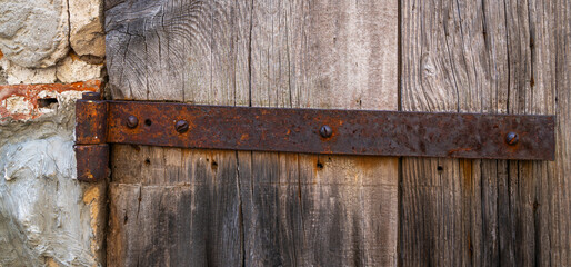 Part weathered wooden door with steel hinges. Distressed wood panels. Castle stone wall texture background. Detail of an old wooden door with paint residues and rusty door latch.