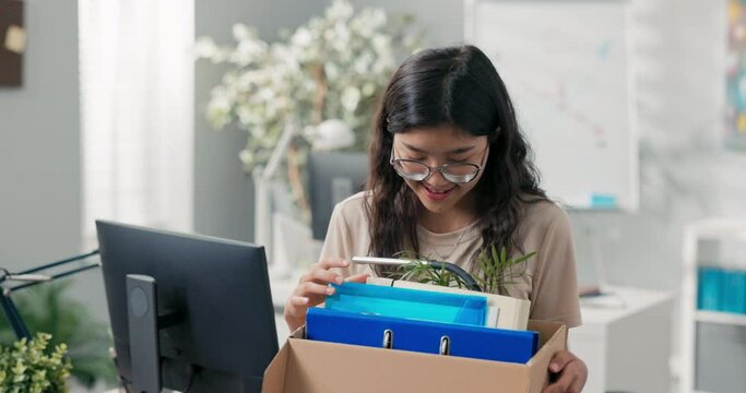 Beautiful woman with Korean Asian beauty gets a promotion in the office, changes position, carries her things packed in a box, moves them, leave job, she is happy smiling, leaves the company