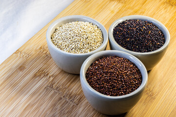 Red, black and white quinoa seeds on wooden background. Vegetarian food